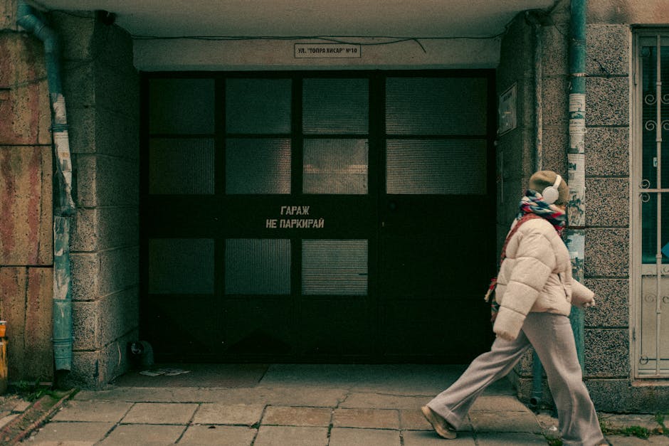 A person walks past an urban garage door with a No Parking sign on a city street.